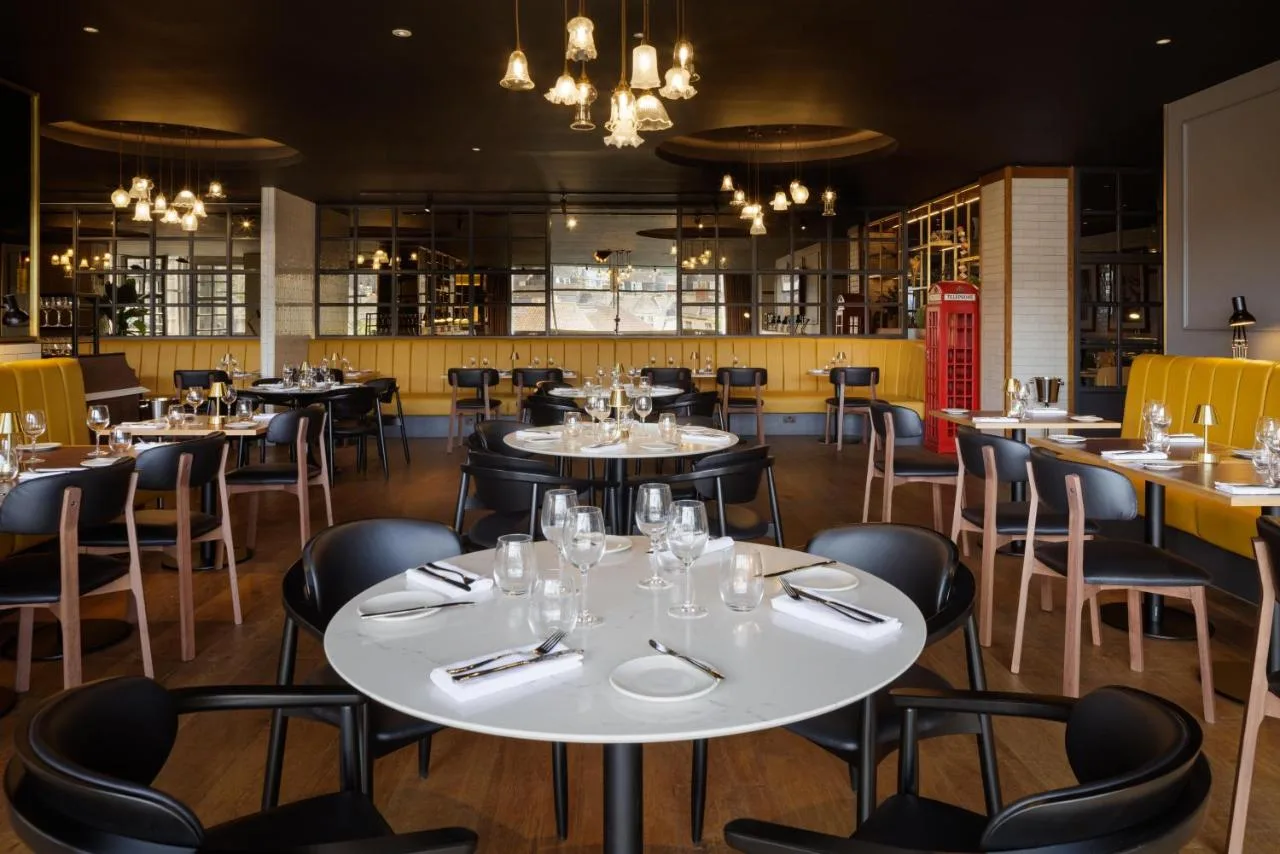 a restaurant with white tables and black chairs at DoubleTree by Hilton Bath in Bath